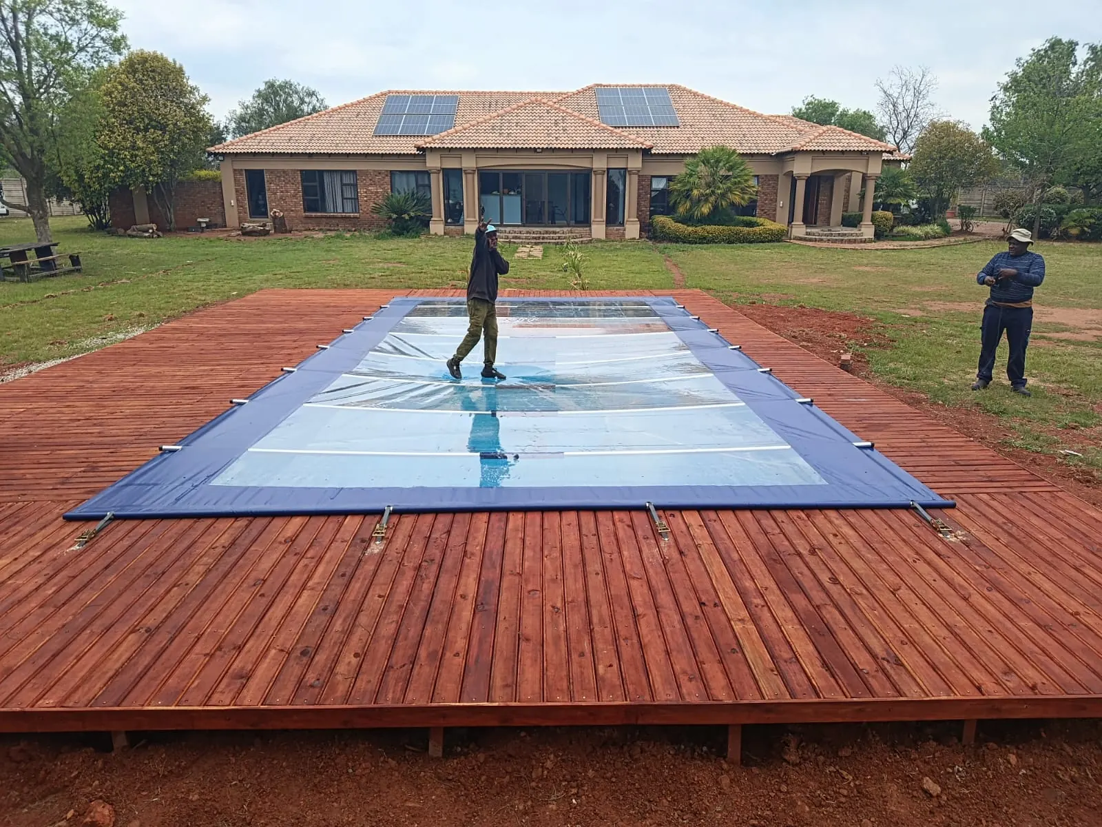 Two men on a clear-panel cover over a pool set in a timber deck