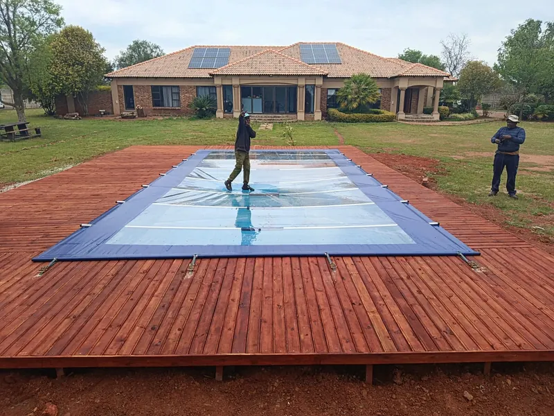 Two men on a clear-panel cover over a pool set in a timber deck