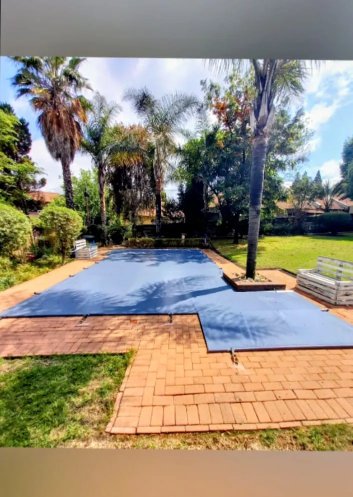 A blue PVC cover on an L-shaped pool in a garden