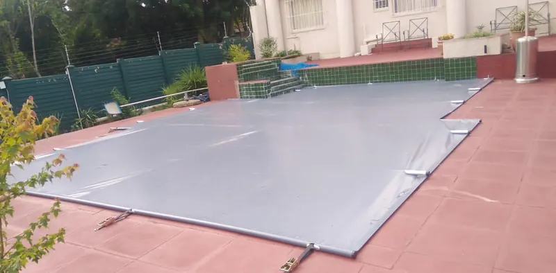 A grey PVC cover over a pool on red paving