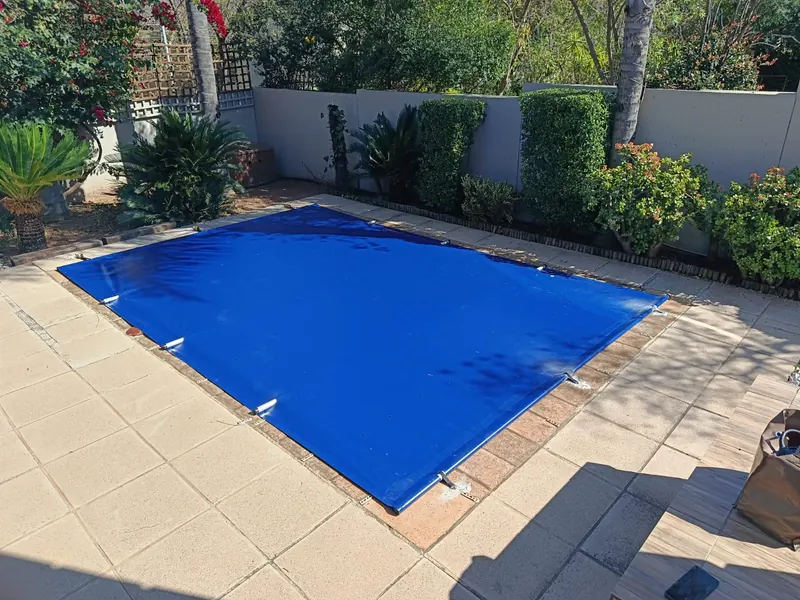 A blue PVC cover strapped over a pool on pale paving