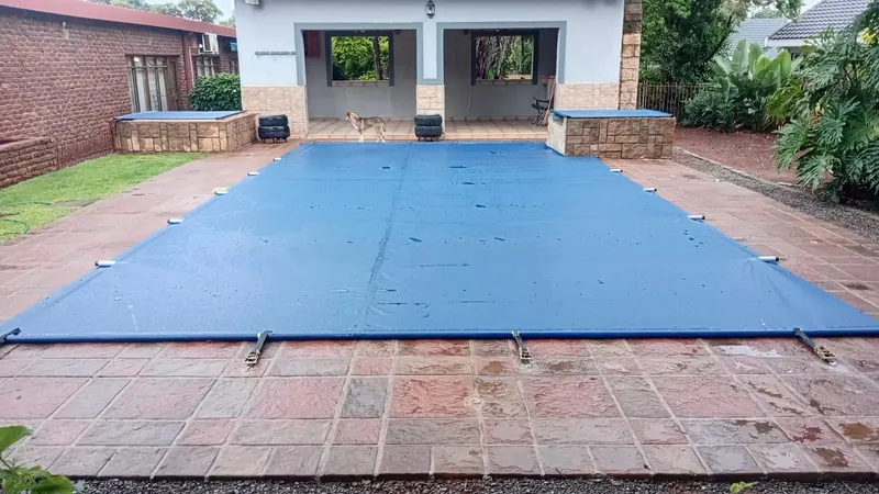 A blue PVC cover over a pool on red paving