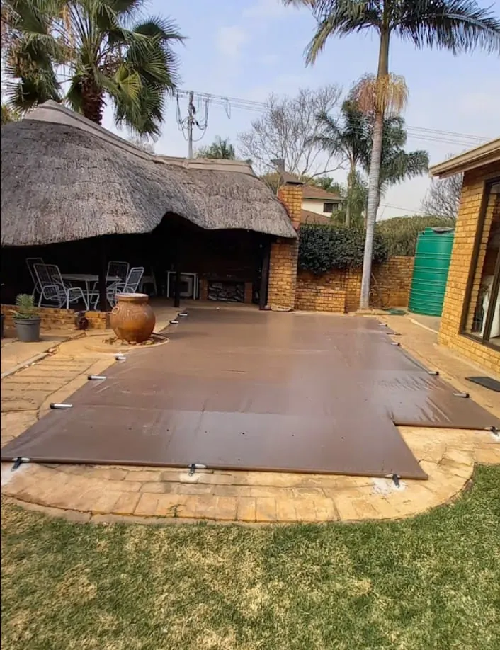 A brown PVC cover on a stepped pool beside a thatched lapa
