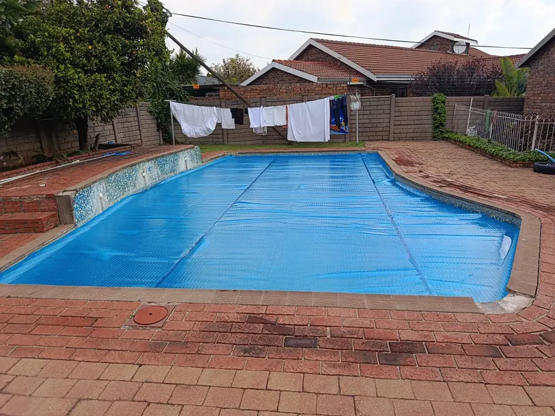 A blue solar blanket on a pool edged with brick paving
