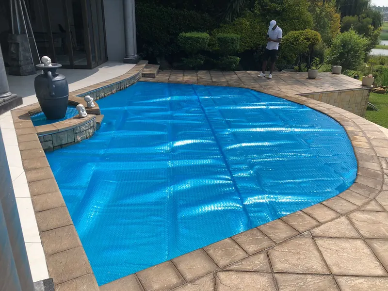 A blue solar blanket on a curved pool beside a fountain